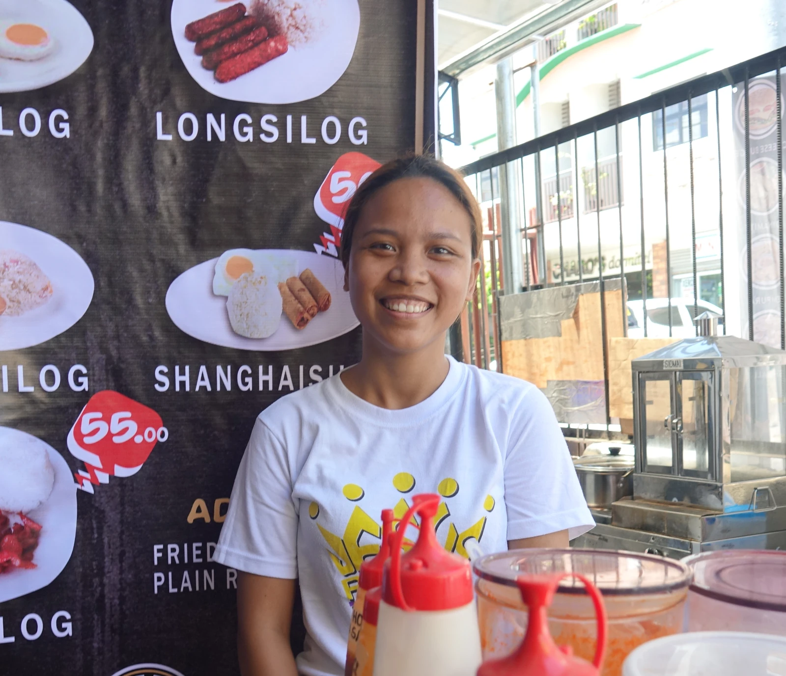 Smiling server for Filipino street food in front of a silog sign.